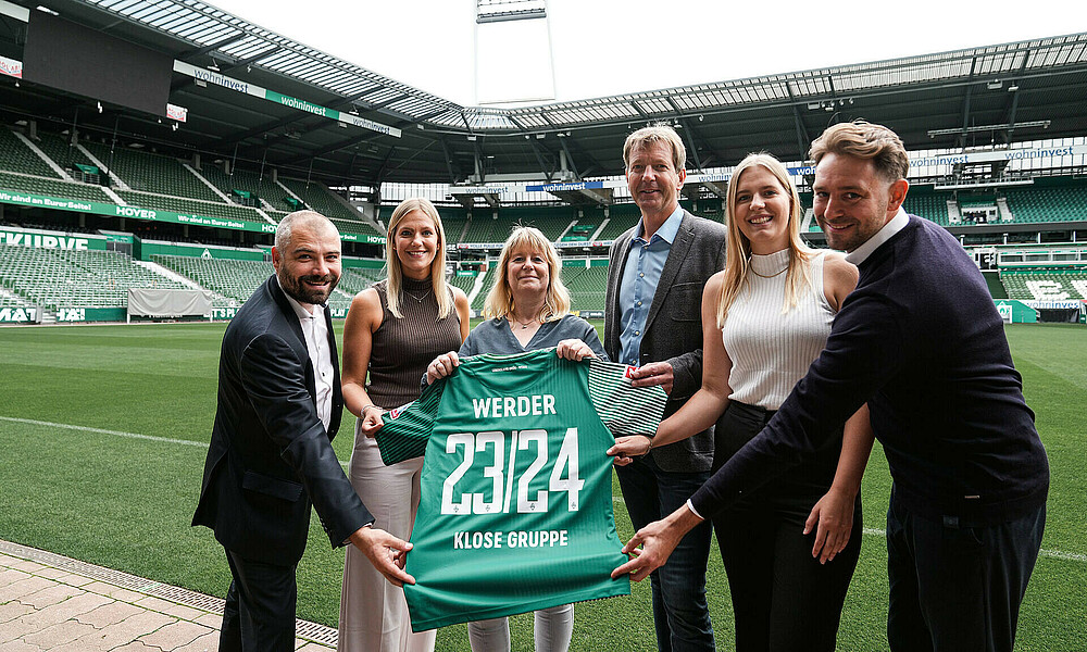 null Vertreter:innen der Firma Klose und von Werder halten zusammen ein Werder-Trikot.