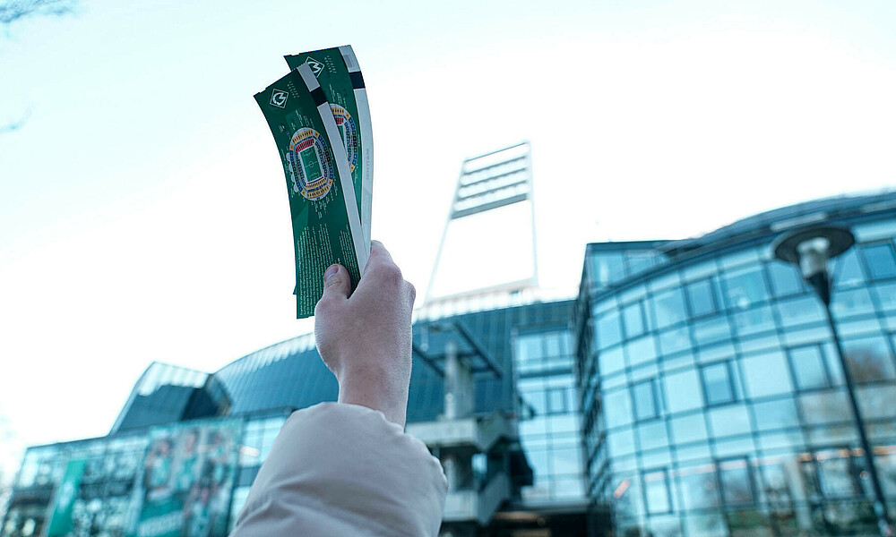 Vor dem Stadion hält ein Mann ein Ticket hoch.