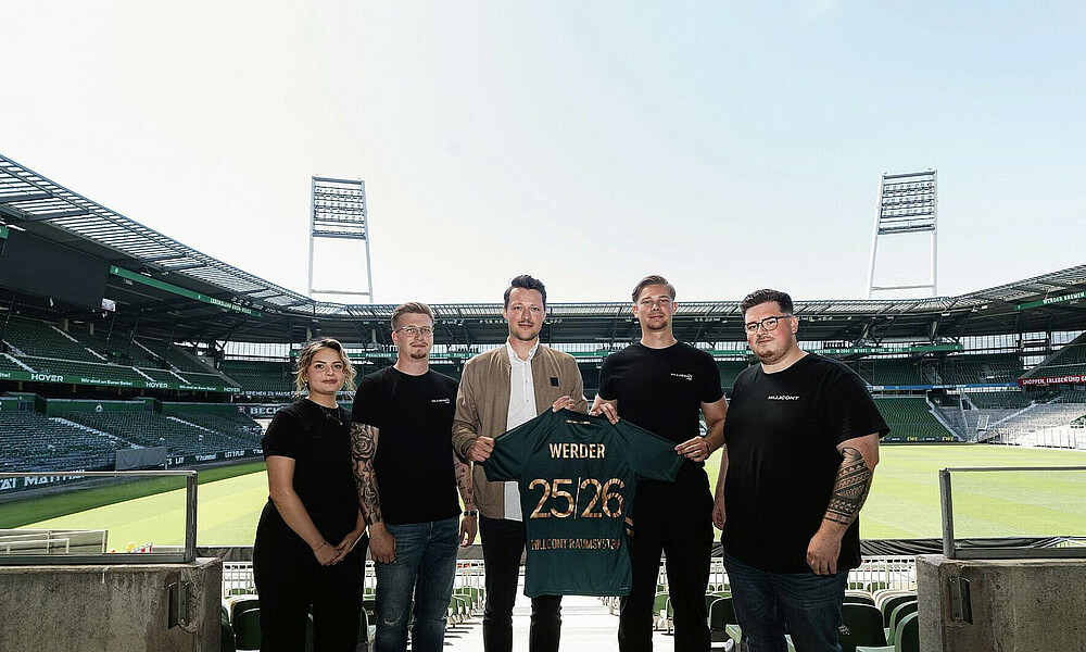 Mitarbeitenden von HILLCONT und Werder Bremen halten im Weserstadion ein Werder-Trikot mit dem Schriftzug HILLCONT 2025/2026 hoch.