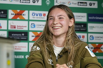 Michelle Weiß lächelt, sitzt vor der Werbetafel in der Mixed Zone. 