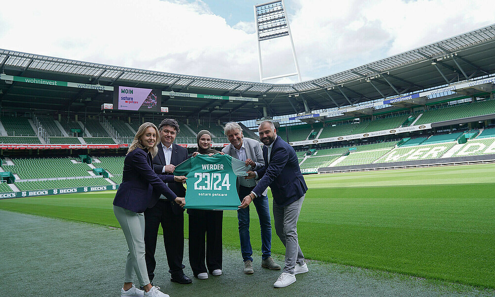 Vertreter:innen von saturn petcare halten ein Trikot mit der Aufschrift saturn petcare 23/24 in die Kamera (Foto: W.DE).