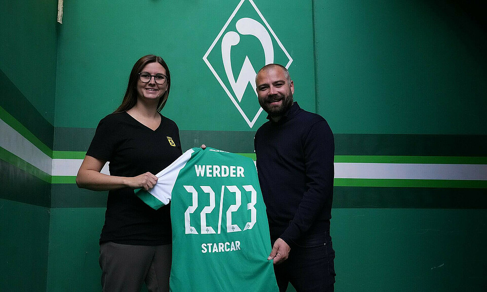 Vertreter:innen von Starcar und Werder halten ein Werder-Trikot vor der Werder-Raute hoch