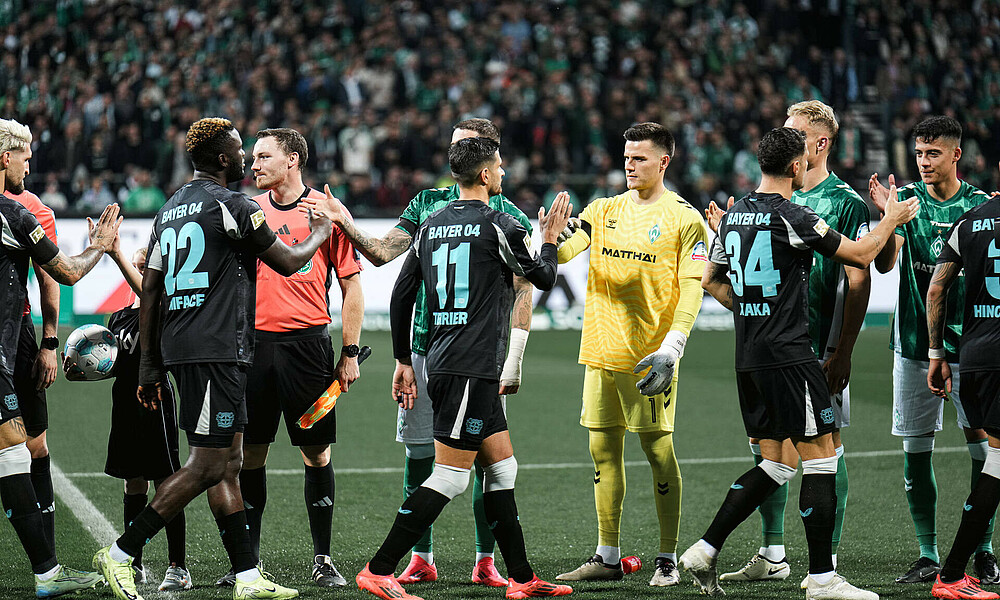 Werder-Mannschaft im Heimtrikot klatscht mit den Leverkusenern zur Begrüßung im Spiel im Weserstadion ab
