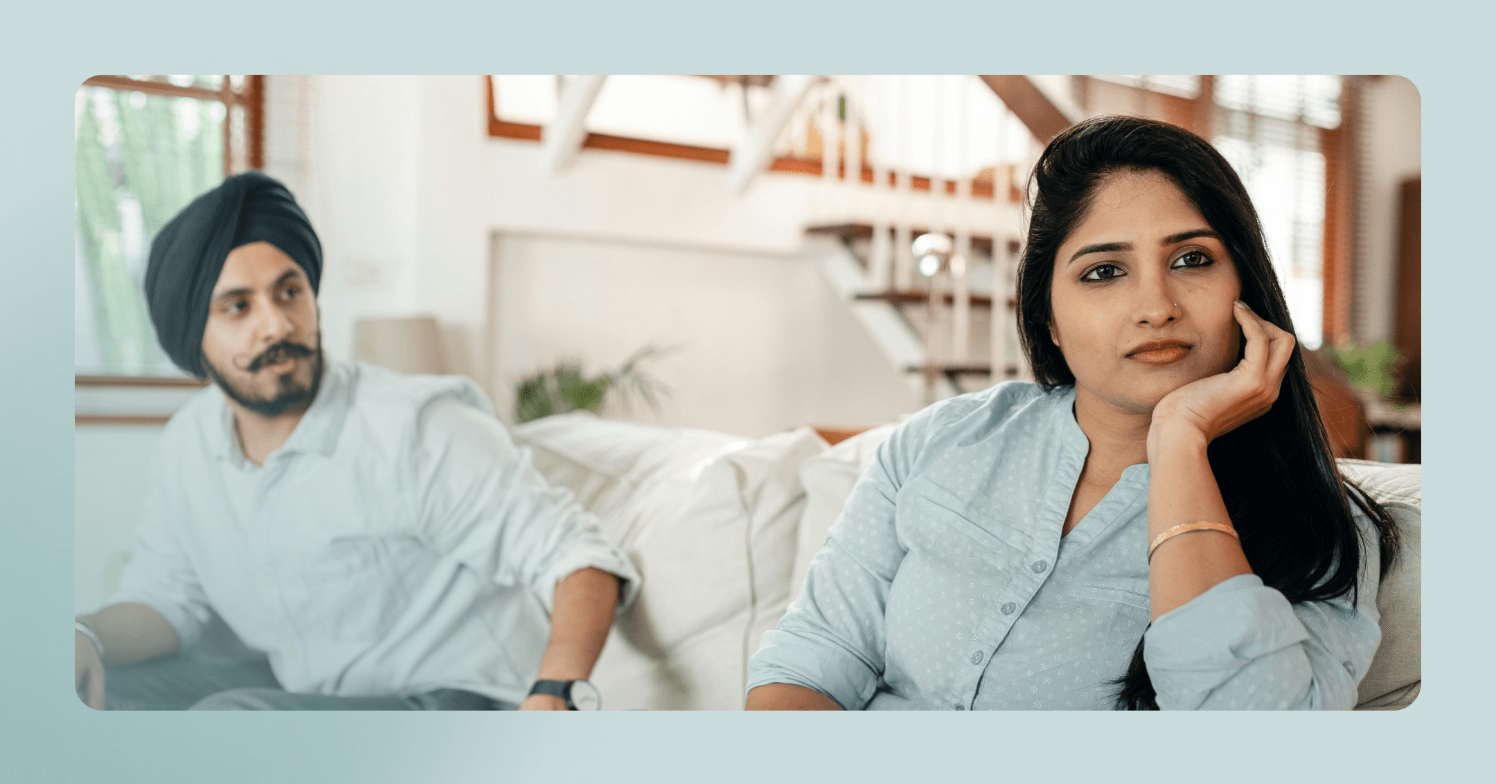 A man and woman are sitting on a couch together. They are sitting at each of the couch and the woman is looking away off camera with a serious look on her face.