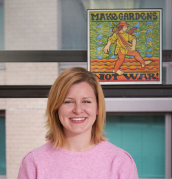 Photo of staff member Alison Baldree in front of poster reading "Make Gardens Not War"