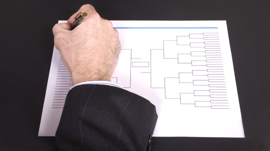 Closeup of a businessman’s hand holding a pen completing tournament bracket