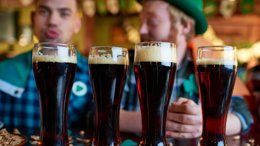 Close-up of full glasses of dark beer with foam placed on table with nut shells