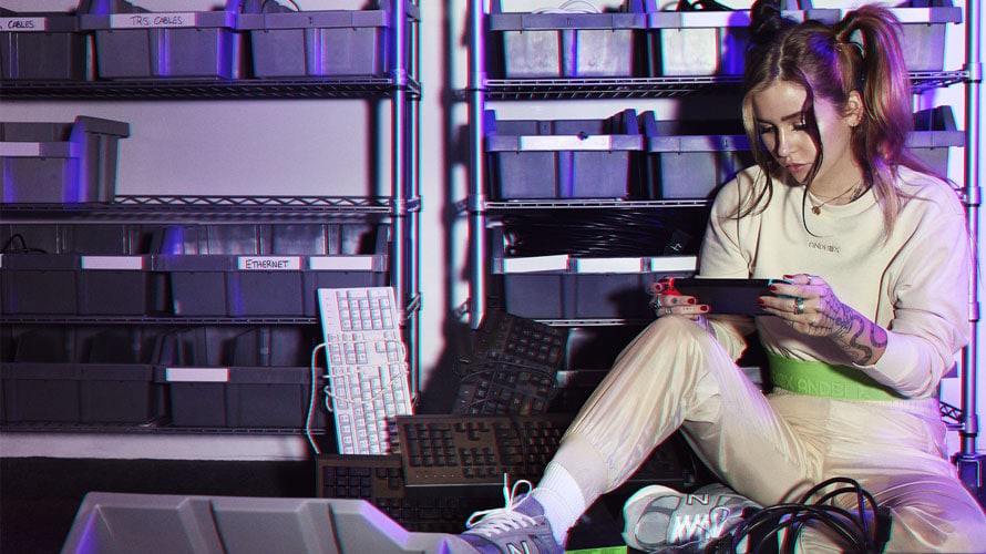 Female model wearing Andbox apparel while playing Nintendo Switch sitting next to a lot of computer equipments