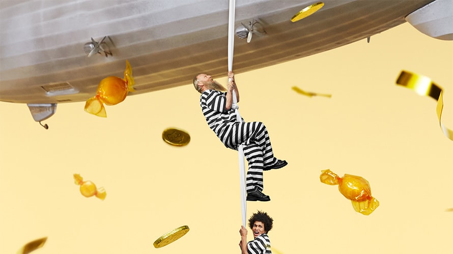 jailblimp-content-2019 Two people in prison stripes climbing a rope into a blimp.