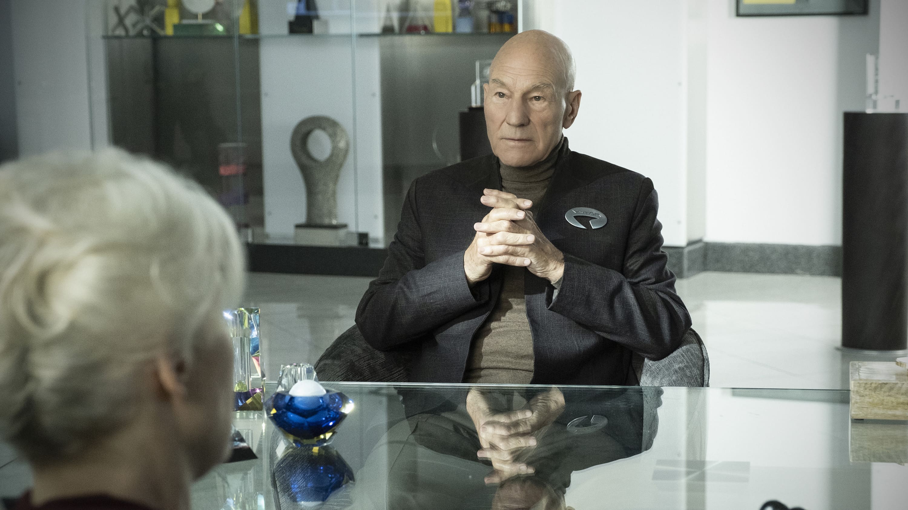 Star Trek: Picard Patrick Stewart from Star Trek sitting at a glass table with his hands clasped.