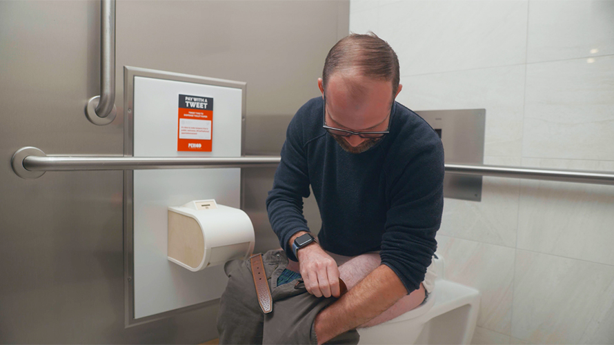 pay-for-toilet-paper-2020 A man on a toilet fumbles for change in his pocket to pay a coin-operated toilet paper dispenser