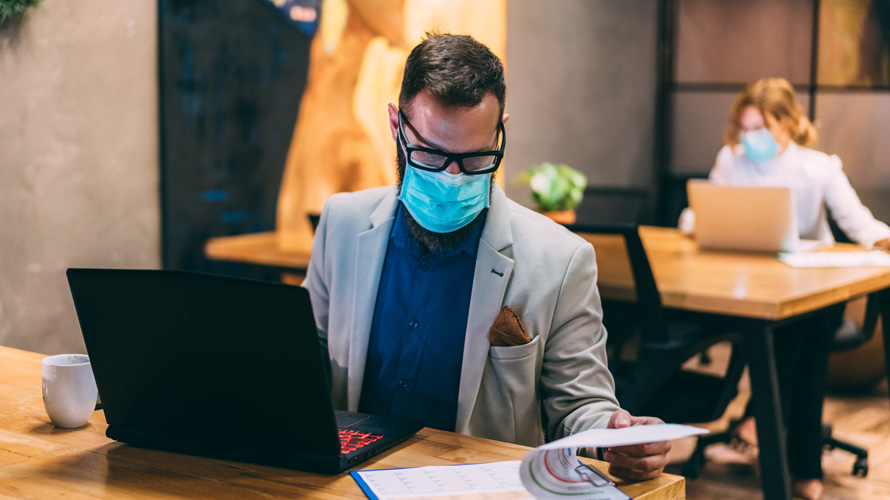 office-return-work-safely-CONTENT-2020 Man wearing a face mask in front of a laptop