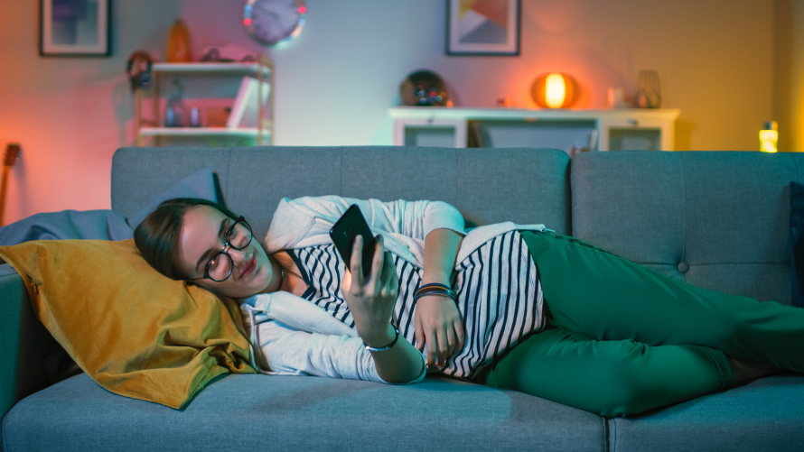 WomanWatchingTVOnCouchHoldingSmartphone