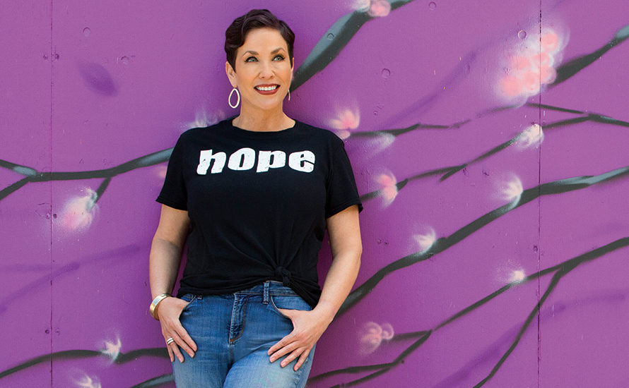 denise-roberson-talent-pool a woman with short brown hair wearing a shirt that says hope, leaning against a purple wall