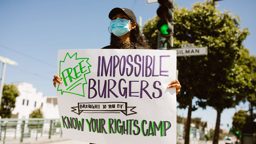 Know Your Rights Camp x IMPOSSIBLE Woman holding up sign for Impossible burgers