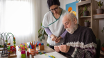 A nurse standing over an elder man with coloring utensils and tactile toys