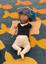 baby lying on blanket facing an open board book