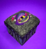 A brightly colored reptilian eye sits nested in felt atop a storage box