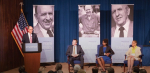 a stage with a speaker at a podium and three more people seated in front of memorial photos