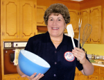 An actress portraying Julia Child holding a bowl and cooking utensils