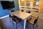 Room with small table, six chairs, and a 50” wall-mounted screen