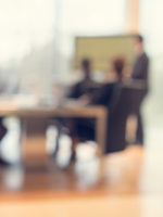 indistinct picture of presenter in front of table with people seated