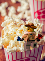 A LEGO mini-figure dressed as a treasure hunter climbs a mountain of buttered popcorn.