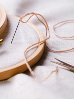 embroidery hoop with cloth, with needle and thread standing up in cloth. Points of scissors showing 