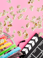 Popcorn kernels, freeze pops, and a director's viewfinder (Take 2!) are scattered atop a cotton cand