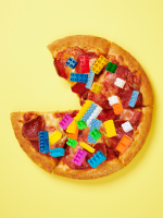 A whole pizza is set against a yellow backdrop. Toppings include pepperoni and LEGO bricks.