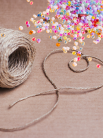 A hemp twine heart rests against a cardboard background. Irridescent seed beads shimmer from the cor