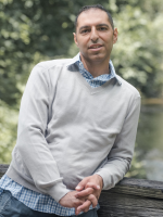 Marc-Anthony Arena leaning casually on stone wall in front of nature background