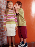 A child listening while another child whispers in their ear