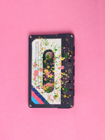 A cassette tape covered in paint splatter in front of a pink background.
