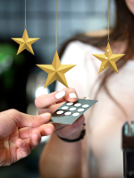 A hand holding a business card-sized loyalty punch-card with golden stars hanging above them.