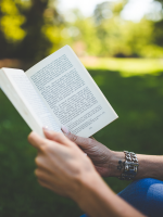 person reading a book under a tree; only person's forearms and book are visible