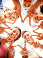 A group of teenagers standing in a circle holding up the two-finger, V-shaped "peace sign" and smili