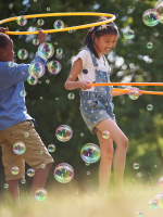 Kids hula-hoop in a field with bubbles.