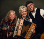Three smiling musicians, a woman with a violin, another with an accordion, and a man in a flat cap. 