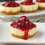 A close-up shot of a mini cheesecake topped with a generous serving of red berry compote. The cheese