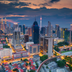 A panoramic view of a city skyline at dusk, with illuminated skyscrapers and the Petronas Twin Tower