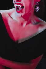 a person in a black dress with vampire fangs, and blood on their face