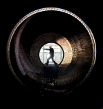 Man pointing a gun at the end of a long tunnel/big pipe