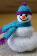 A needle felted snowman in a blue hat and scarf.