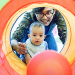 baby and adult male look into tunnel with ball