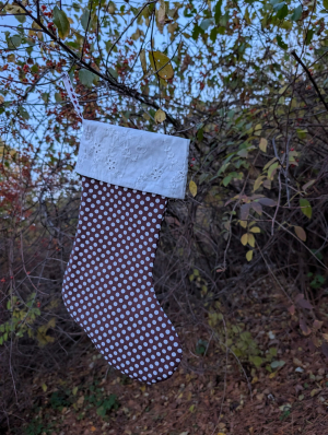 A brown and white polka dot stocking with white trim hanging on a tree branch outdoors