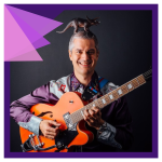 musician Matt Heaton, a white-presenting, middle-aged man, smiles with his guitar while balancing a 