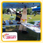 librarian Julie smiles with a blow-up alpaca underneath a pop-up canopy, outside on the Burlington T