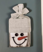 2x4 painted white with a snowman face and a knitted glove as the hat
