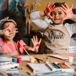 A photo of two kids with messy hands from painting.